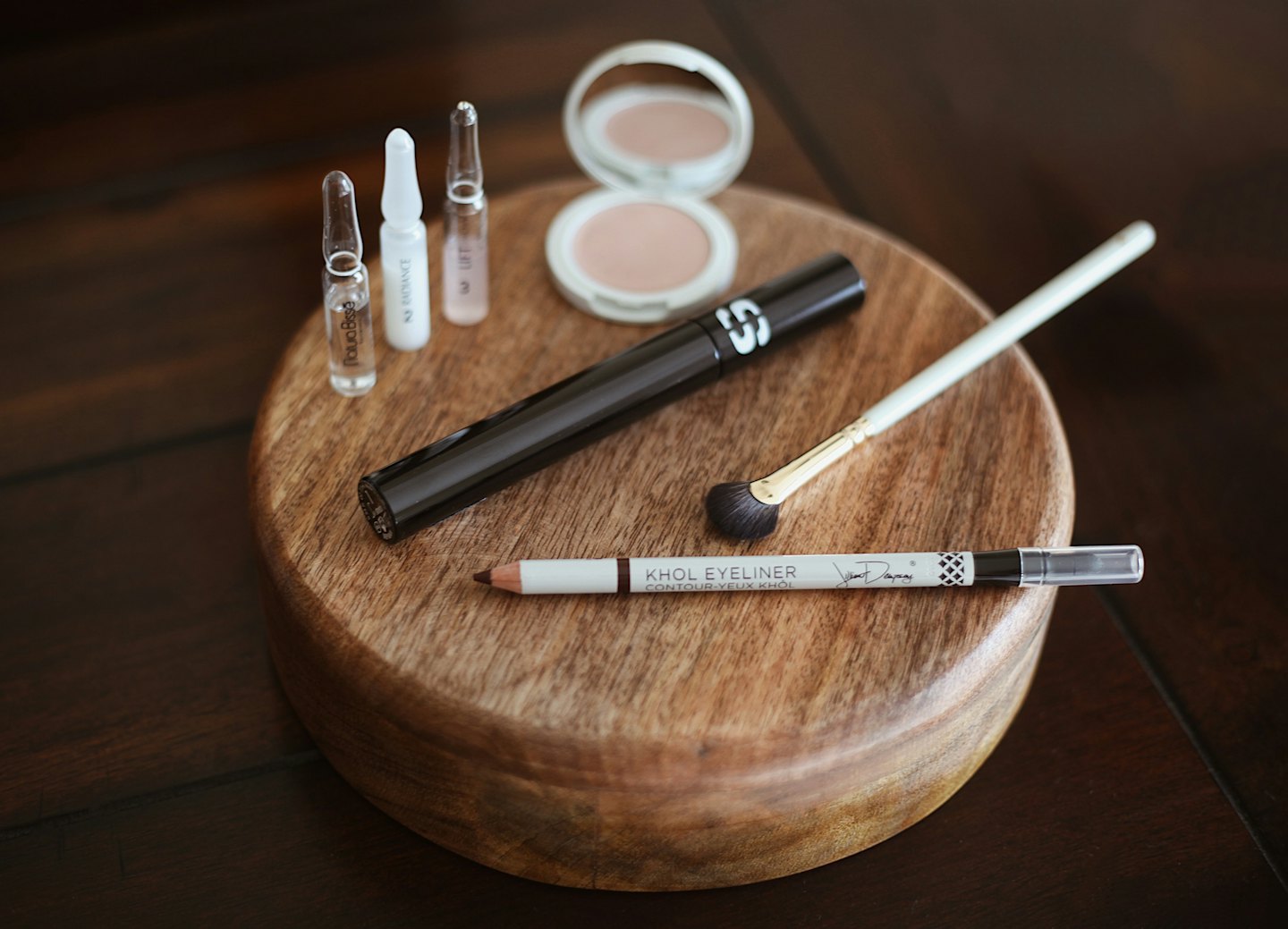 Various makeup and skincare products on a wooden platter.